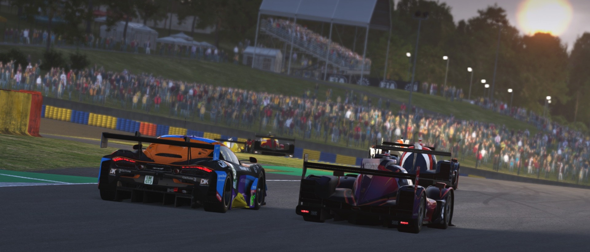 A GT3 car and two prototypes racing towards the grandstands at Le Mans at sunset in Le Mans Ultimate, with crowds lining the circuit.