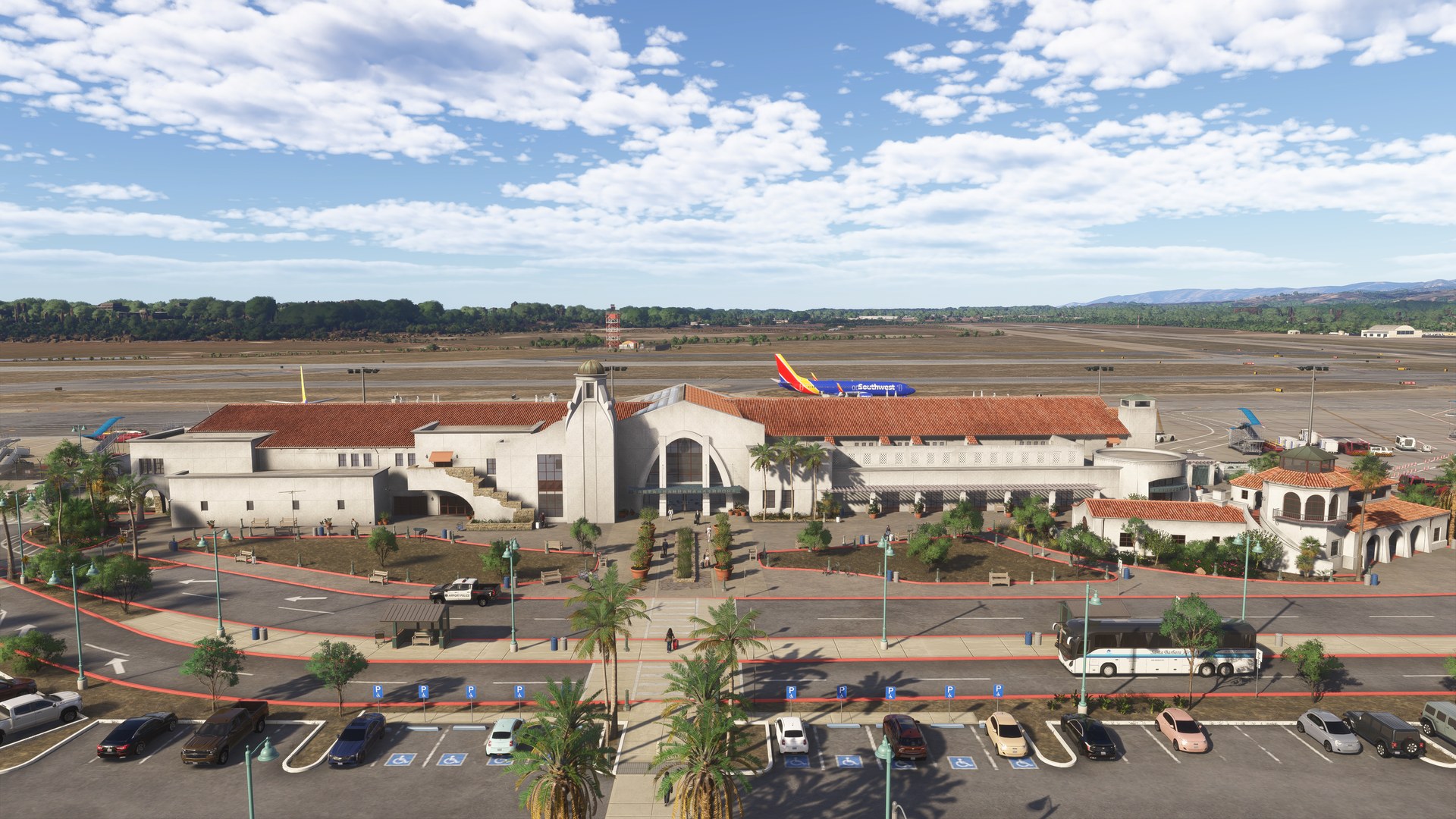 An aerial view of Santa Barbara Airport's red-roofed terminal, car parks and apron, with hills behind